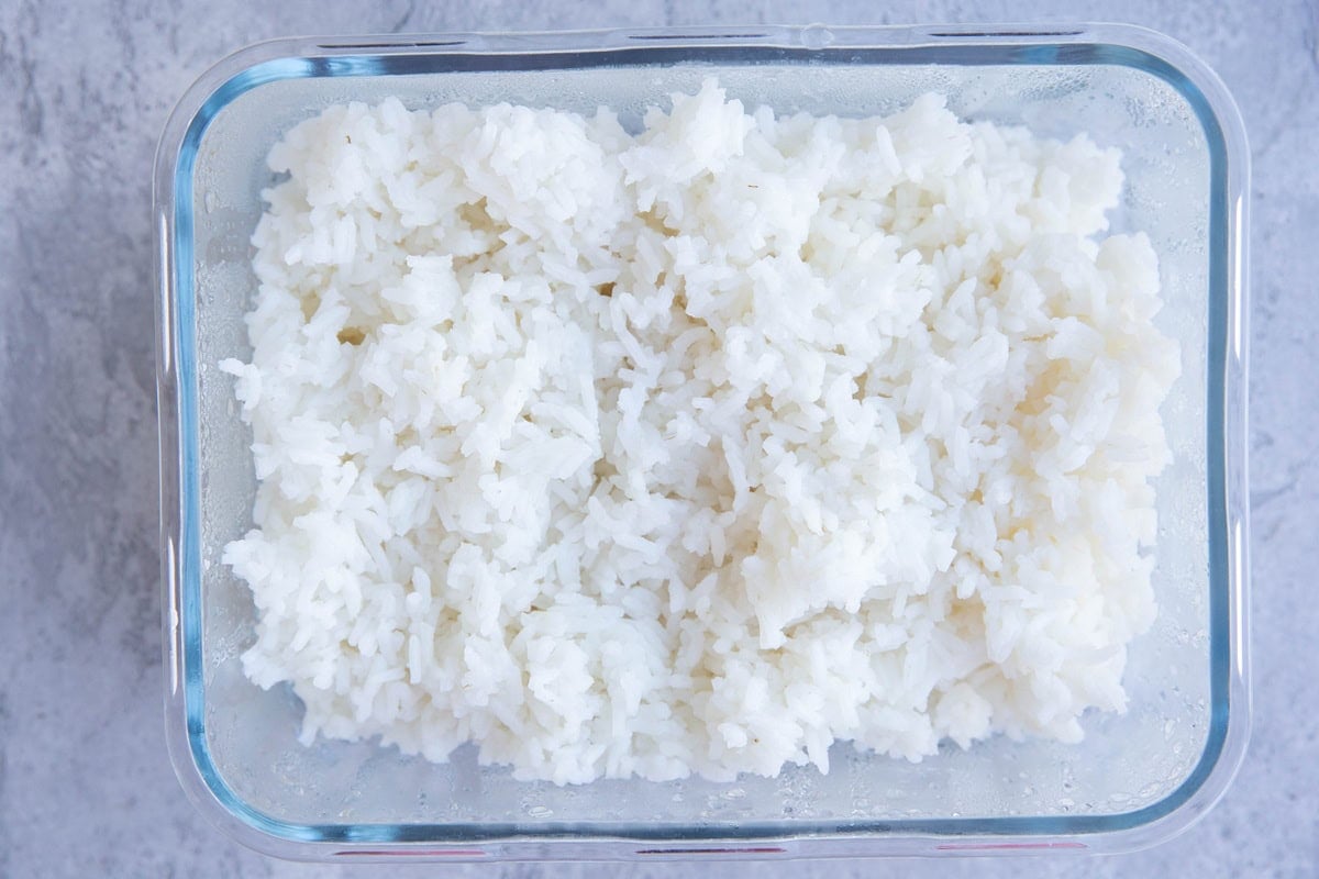 Cooked rice in a glass storage container. One day old leftover rice to make fried rice.