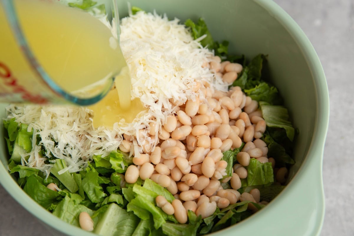 Pouring lemon dressing into the bowl with the lettuce, beans, and cheese.