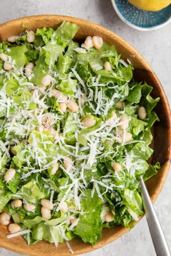 Wooden bowl full of romaine lettuce, parmesan cheese, and white beans dressed with lemon dressing.