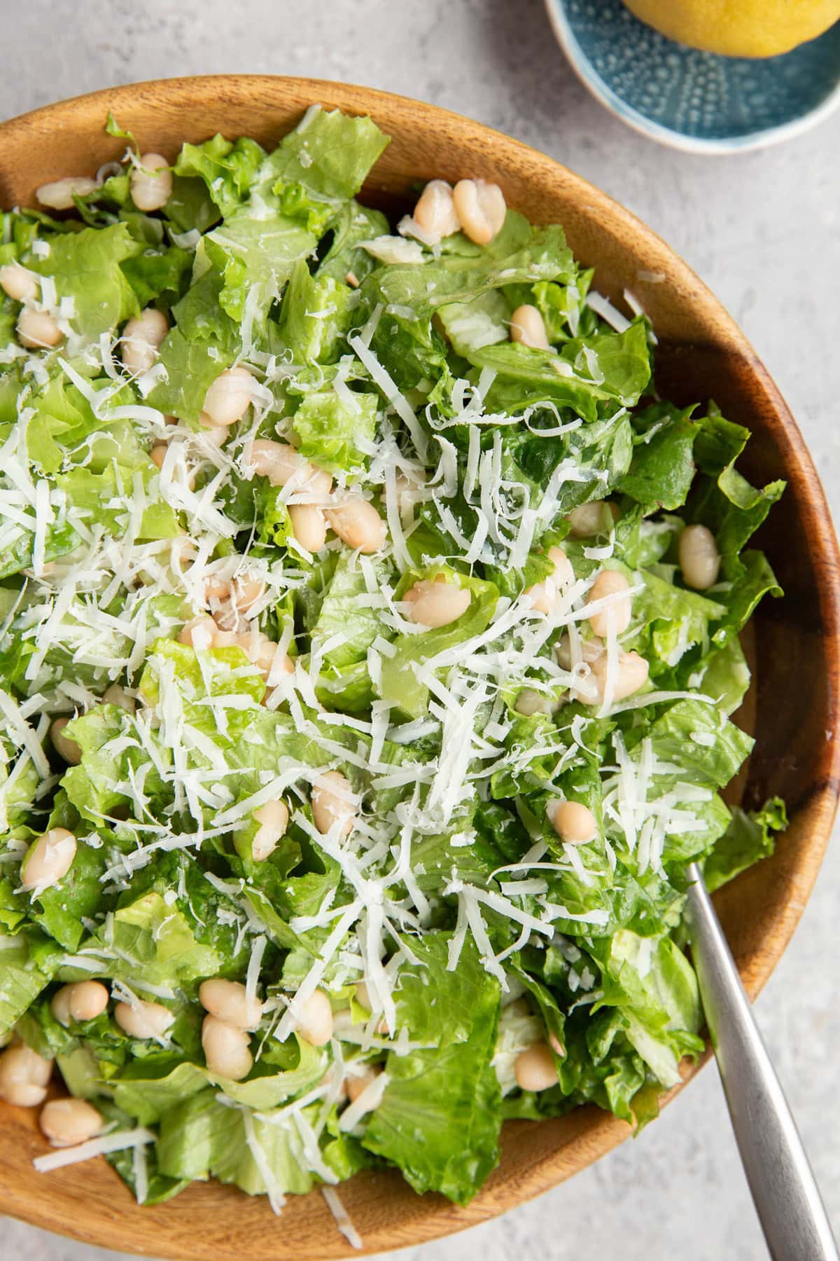 Wooden bowl full of romaine lettuce, parmesan cheese, and white beans dressed with lemon dressing.