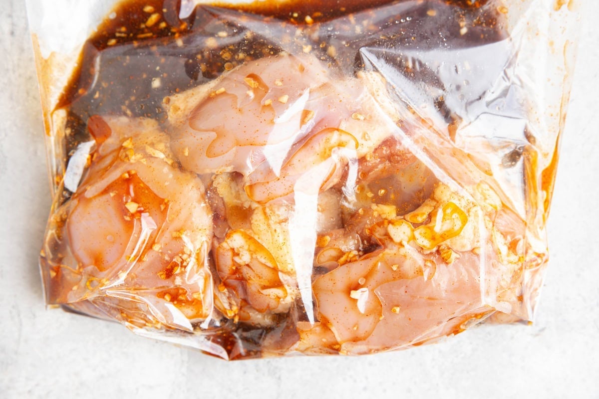 Large zip lock bag full of raw chicken thighs sitting in a dark colored chicken marinade.