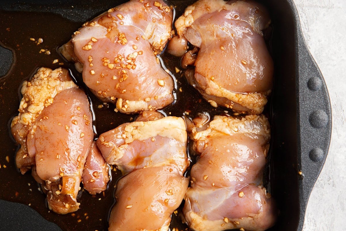 Casserole dish full of raw marinated boneless chicken thighs and the marinade, ready to go into the oven.