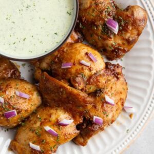 Peruvian chicken on a white plate with a bowl of green sauce to the side.