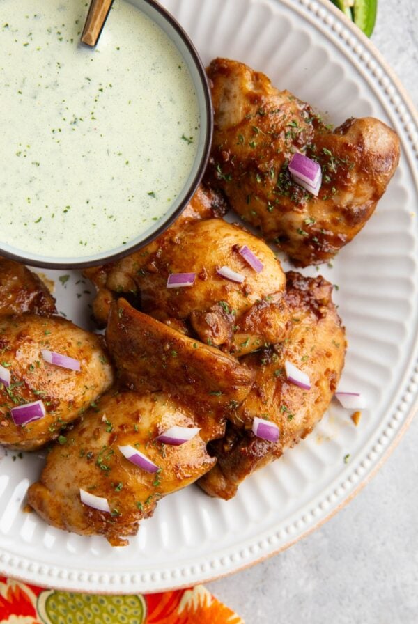 Peruvian chicken on a white plate with a bowl of green sauce to the side.