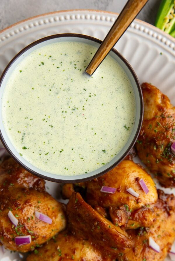 Bowl of green sauce sitting on a plate with Peruvian chicken. Sauce is ready to serve with the chicken.