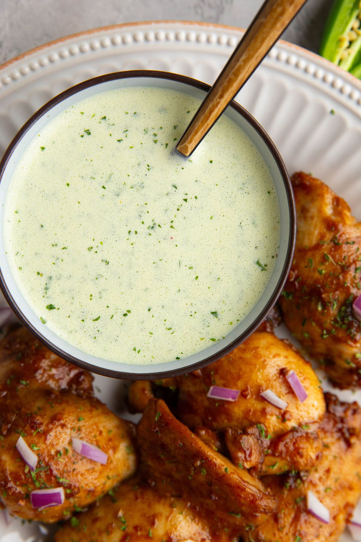 Bowl of green sauce sitting on a plate with Peruvian chicken. Sauce is ready to serve with the chicken.