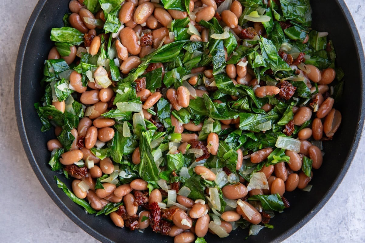 Skillet with pinto beans, collard greens, onion, garlic, and sun-dried tomatoes.