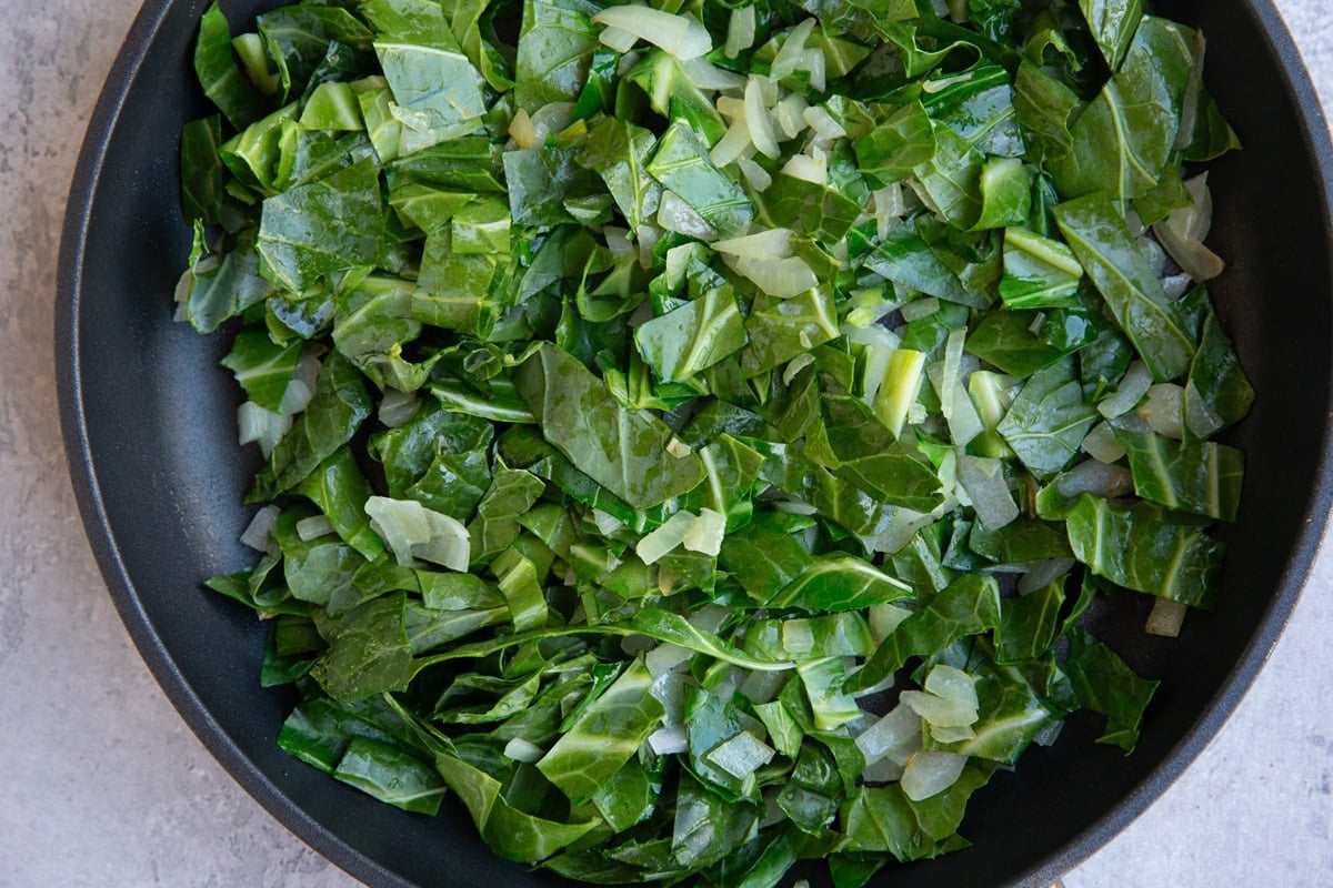 Skillet with sauteed onion, garlic and chopped collard greens, cooking to soften.