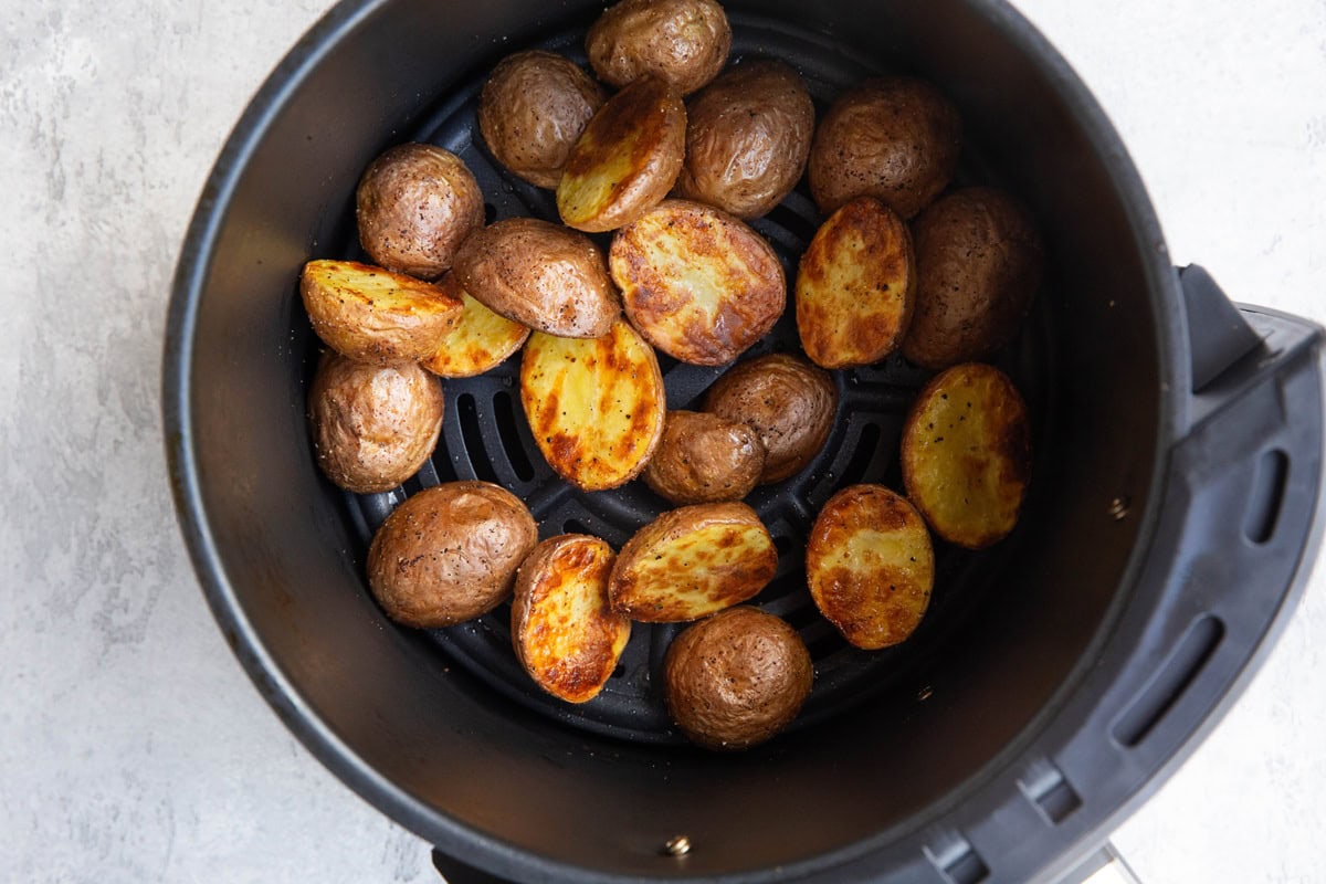 Golden brown baby potatoes in an air fryer that have a golden crust and are finished cooking, ready to serve.
