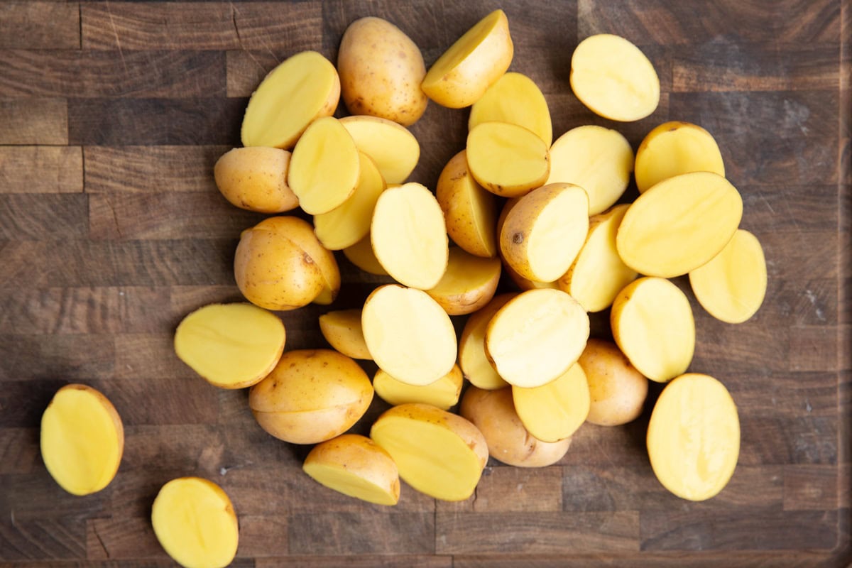 Wooden cutting board with a pile of baby potatoes that have been cut in half.