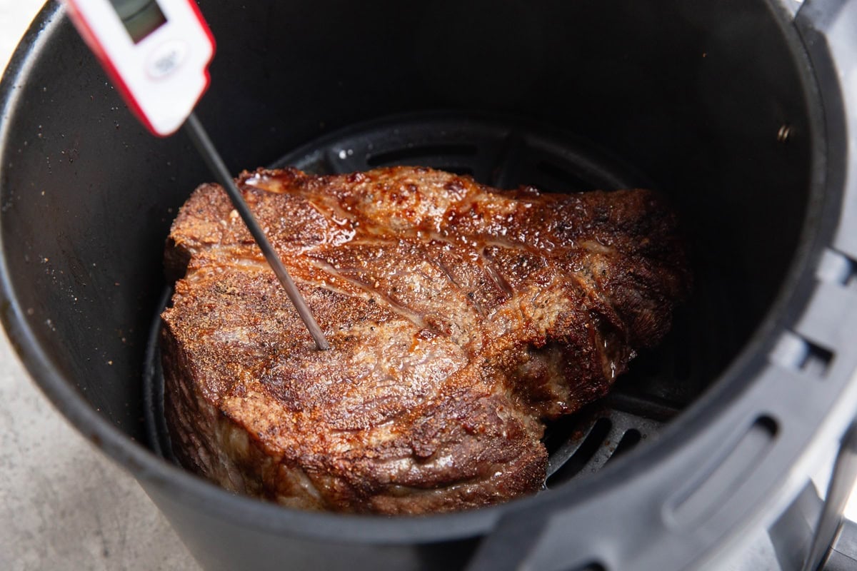 Chuck roast inside of an air fryer that has been partially cooked and is golden brown with a thermometer inserted to take the temperature.