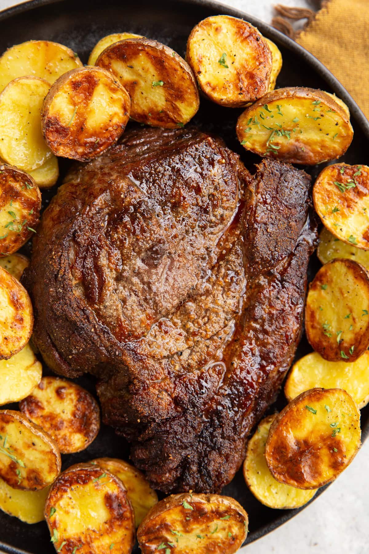 Chuck roast on a black plate with golden cooked potatoes surrounding it, ready to serve.
