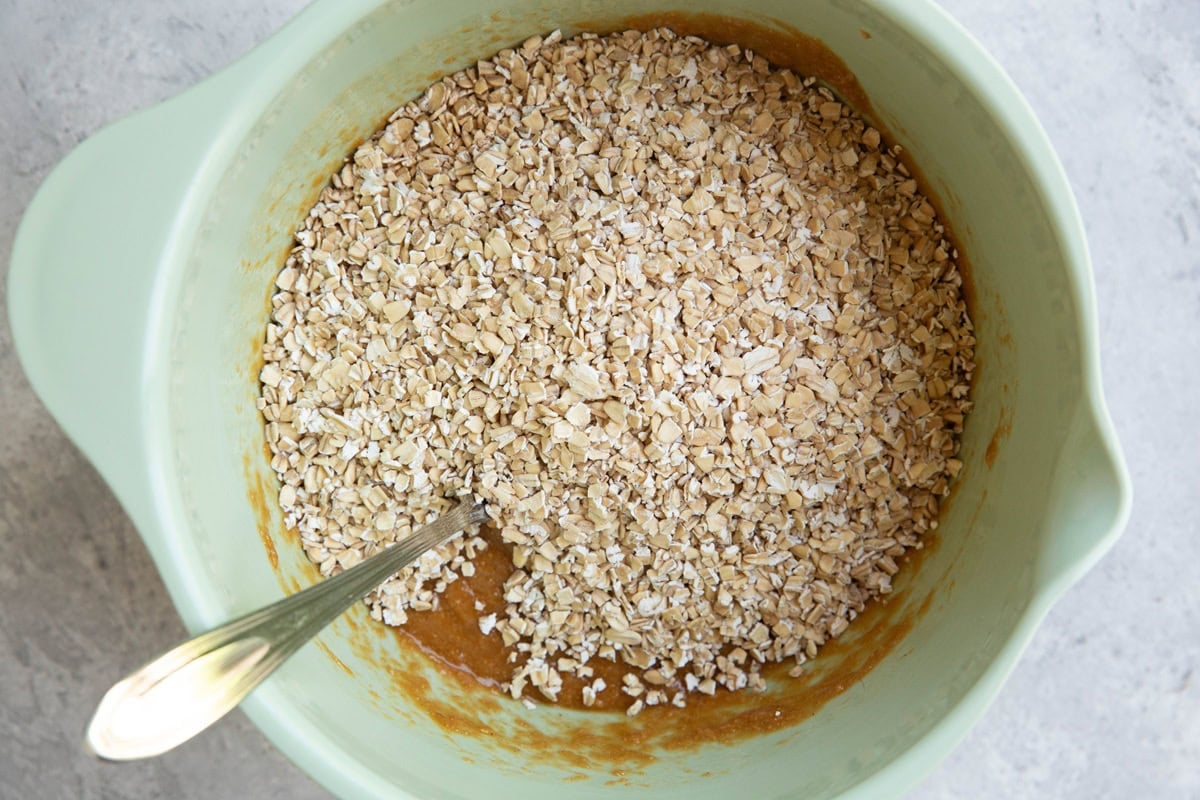 Pale green mixing bowl with wet ingredients on the bottom and oats on top, ready to be mixed in.
