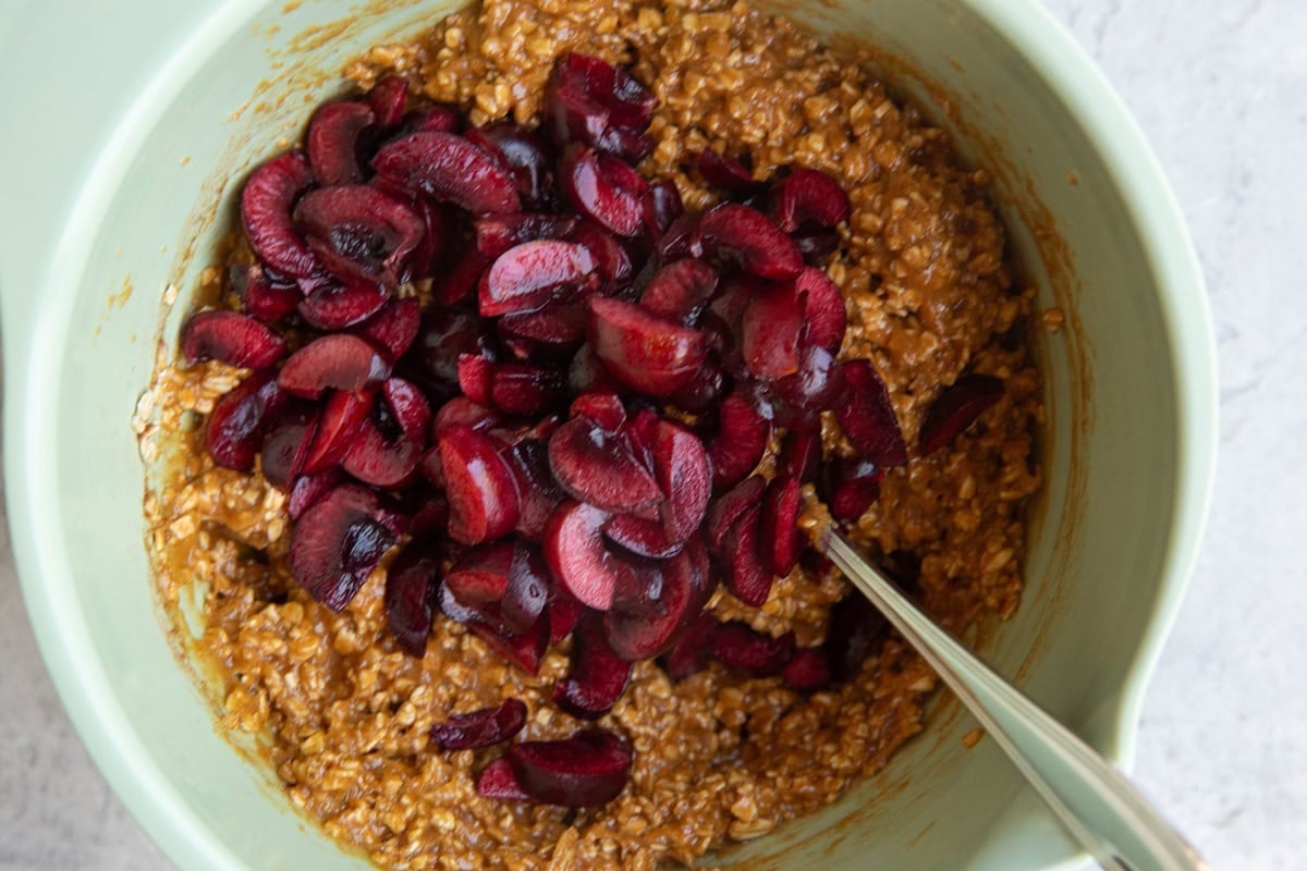 Chopped cherries on top of oatmeal cookie dough inside of a mixing bowl, ready to be mixed in.