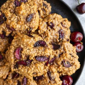 Cherry oatmeal cookies on a black plate with fresh cherries all around.