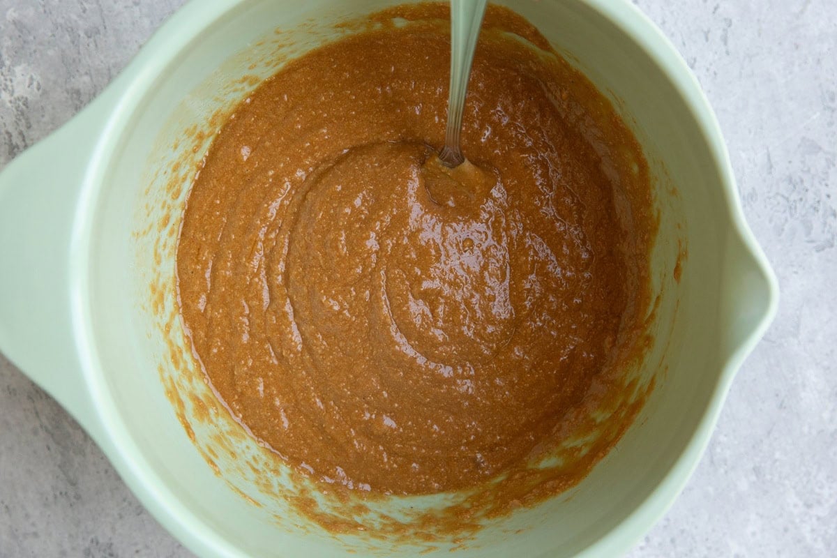 Almond butter, eggs, and pure maple syrup mixed into a creamy consistency in a pale green mixing bowl with a fork.