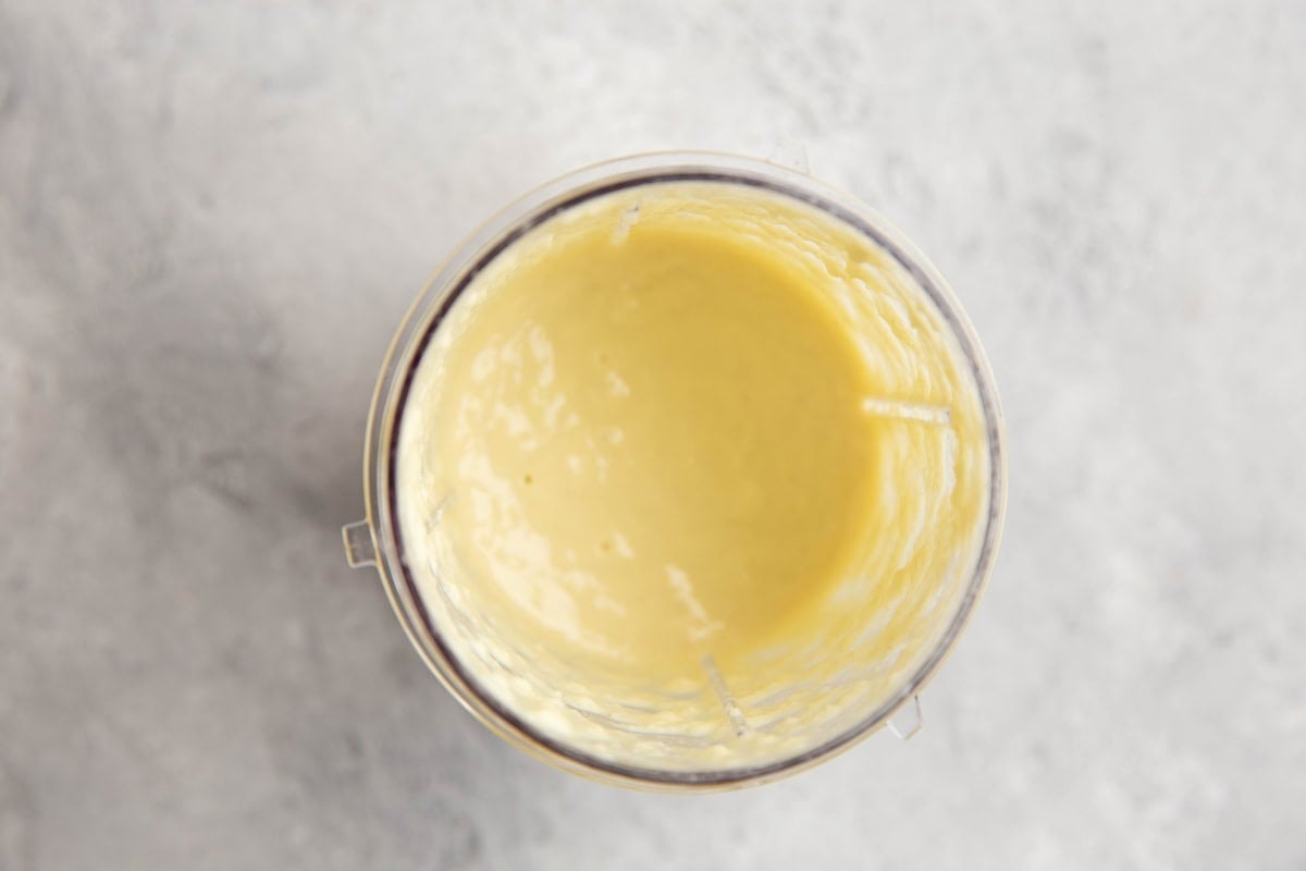 Small blender with creamy Caesar salad dressing inside.