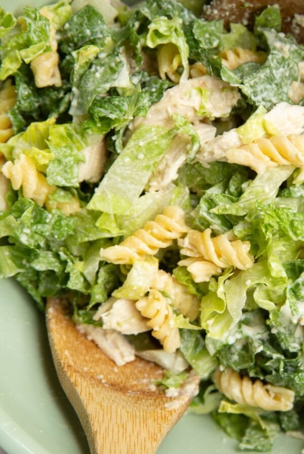 Chicken Caesar pasta salad in a large mixing bowl with two wooden spoons, ready to serve.