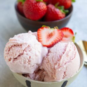 Strawberry cottage cheese ice cream in a cream colored bowl with another bowl of fresh strawberries in the background.