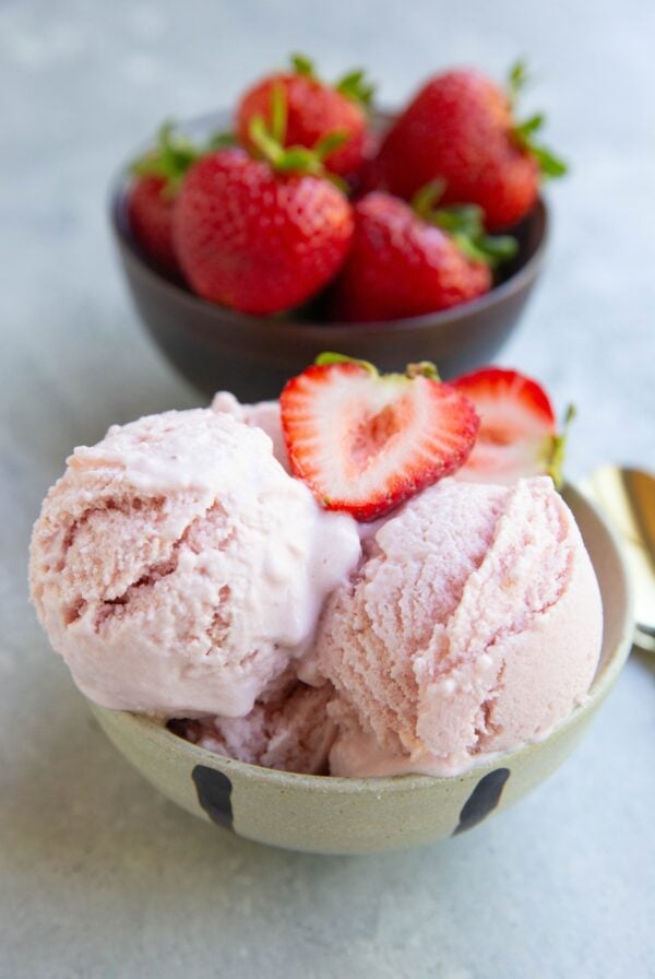 Strawberry cottage cheese ice cream in a cream colored bowl with another bowl of fresh strawberries in the background.