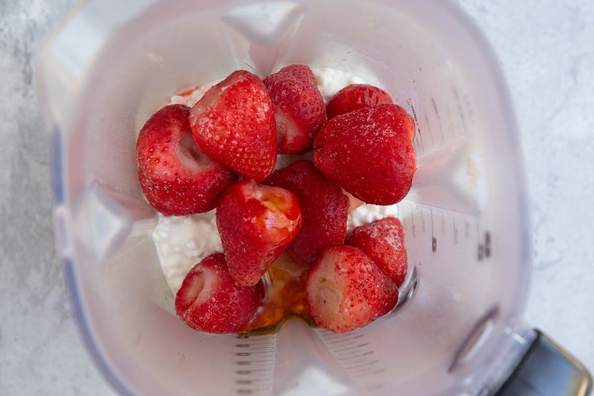 High-powered blender with cottage cheese, pure maple syrup, and fresh strawberries inside, ready to blend into a creamy consistency.