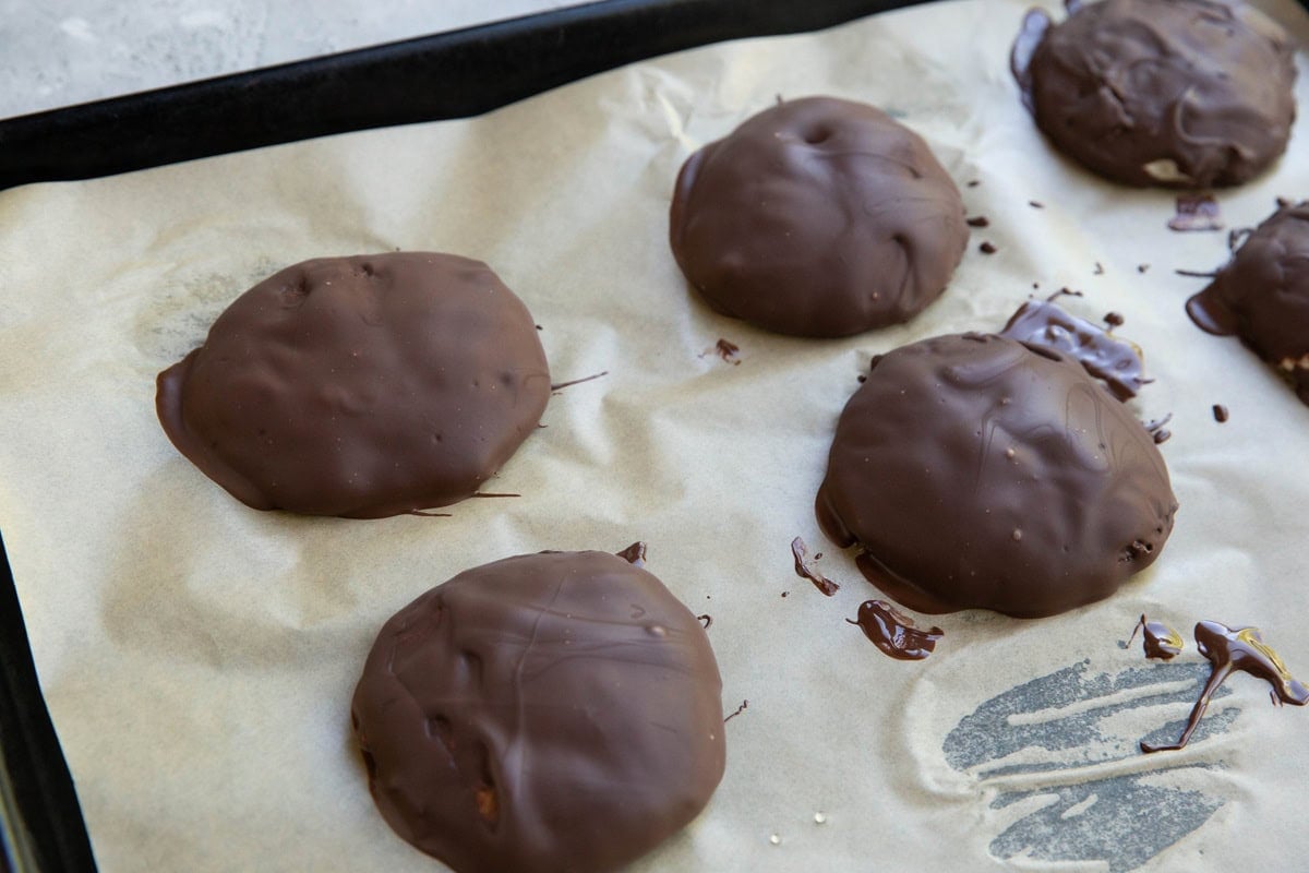 Chocolate covered mounds of frozen yogurt on a baking sheet lined with parchment paper, ready to go back into the freezer.