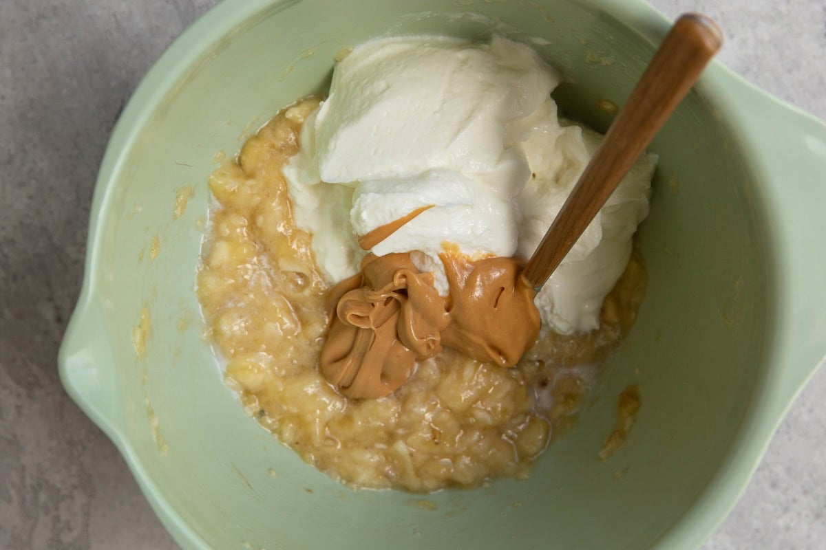 Mixing bowl with mashed banana, peanut butter, and Greek yogurt, ready to be mixed together.