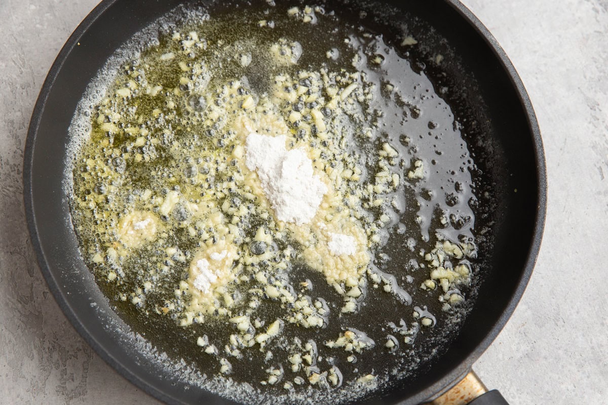 Skillet with melted butter, sauteed garlic and flour added in on top, to be mixed in.