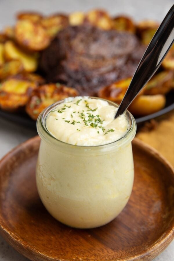 Garlic Butter Sauce in a jar sitting on a wooden plate with a plate of steak and potatoes in the background, ready to be used.
