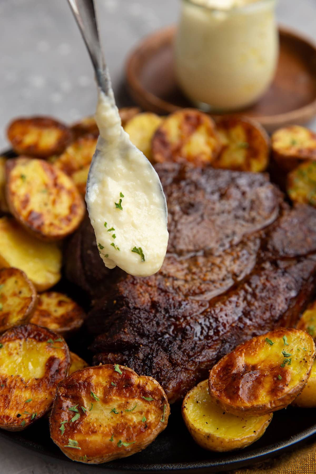 Spoon drizzling some creamy garlic butter sauce over a large hunk of chuck roast with golden brown potatoes all around.