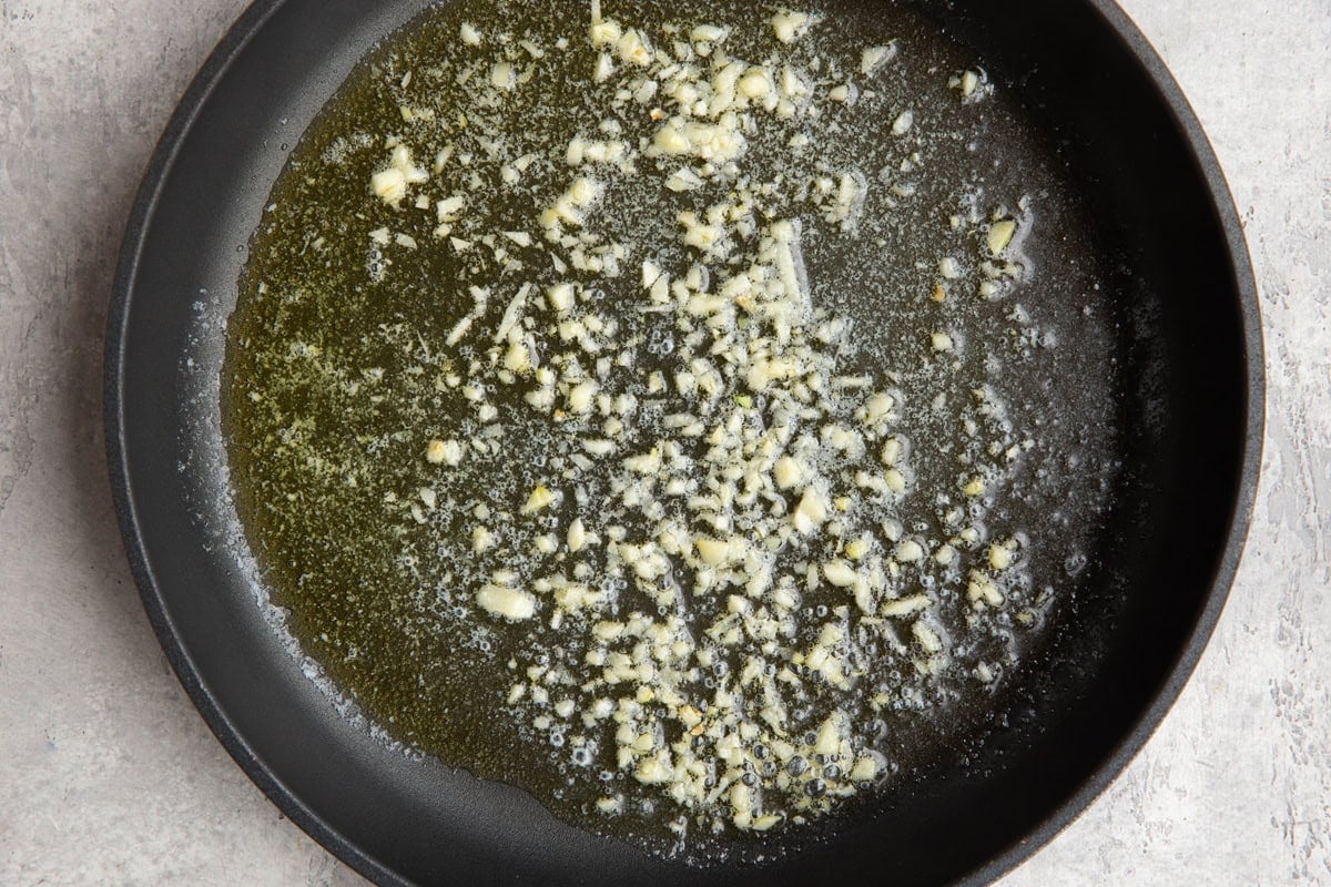 Skillet with melted butter and minced fresh garlic sautéing.