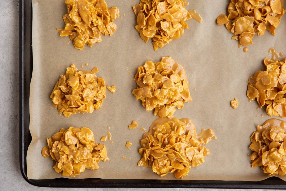 Clusters of golden cornflake cookies are arranged on a parchment-lined baking tray, ready to cooled.