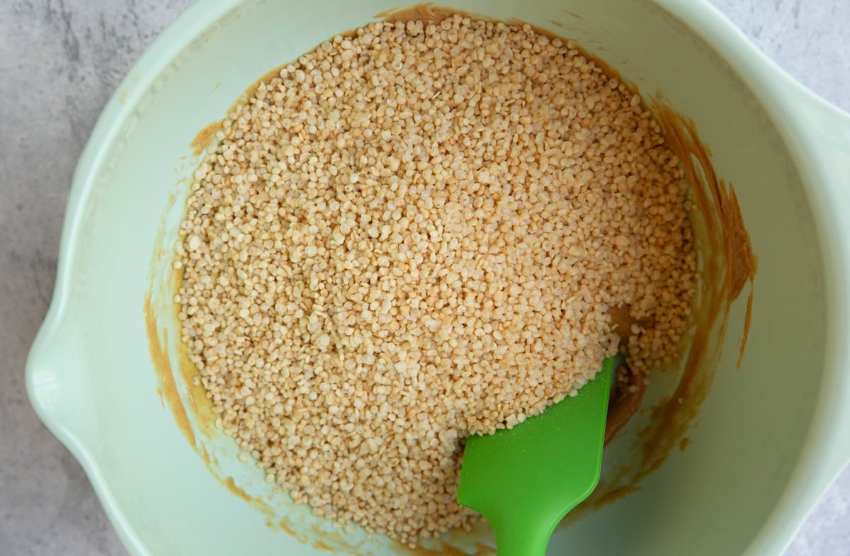 Mixing bowl with peanut butter mixture on the bottom and puffed quinoa on top, ready to be mixed together.