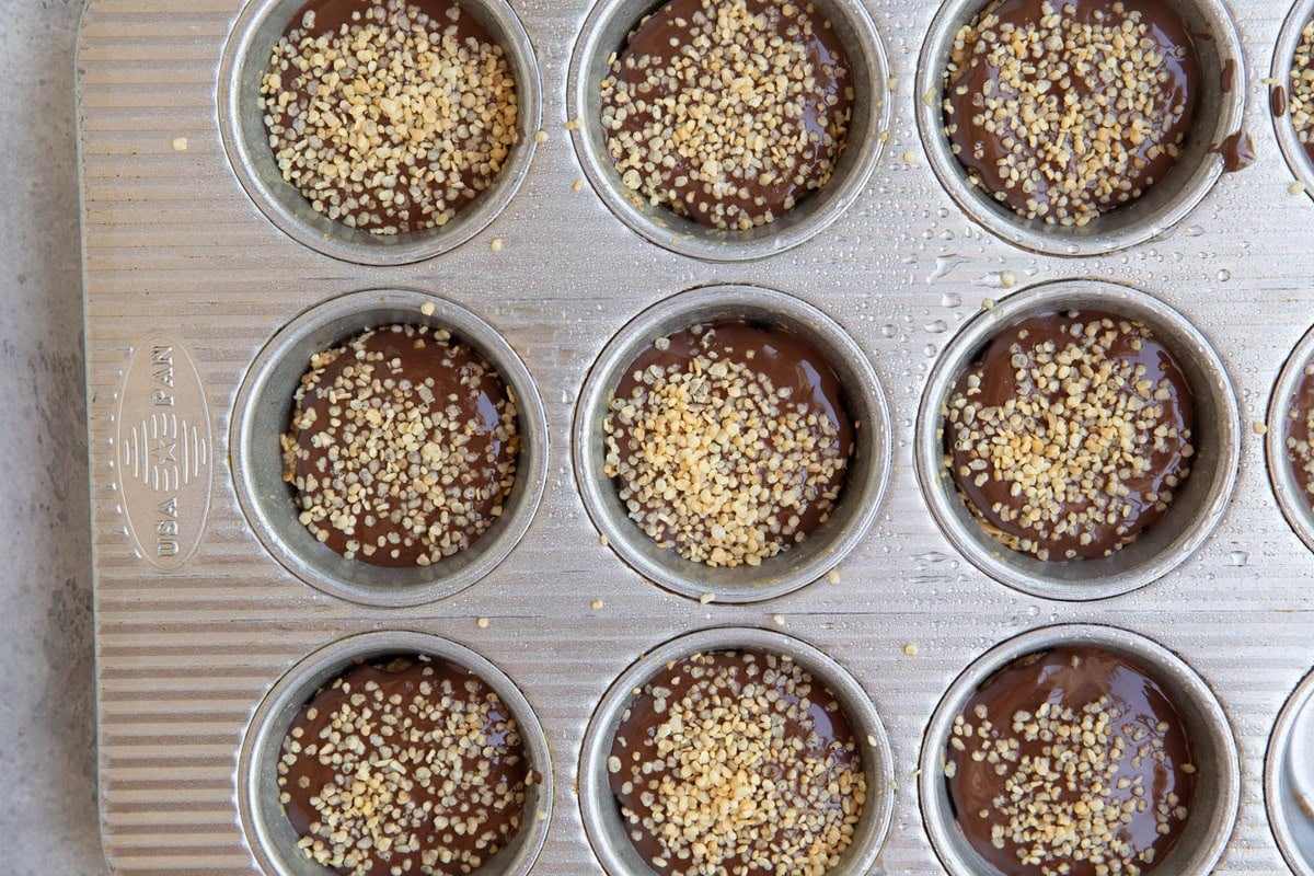 Melted chocolate with puffed quinoa on top of a peanut butter crunchy quinoa layer to make peanut butter cups.