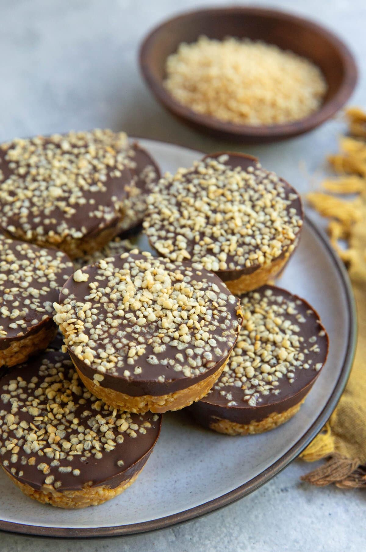 Plate of crispy quinoa peanut butter cups with a golden napkin to the side and a small bowl of puffed quinoa in the background.