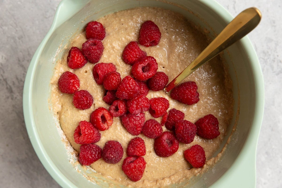 Mixing bowl with muffin batter and fresh raspberries on top, ready to be mixed in.
