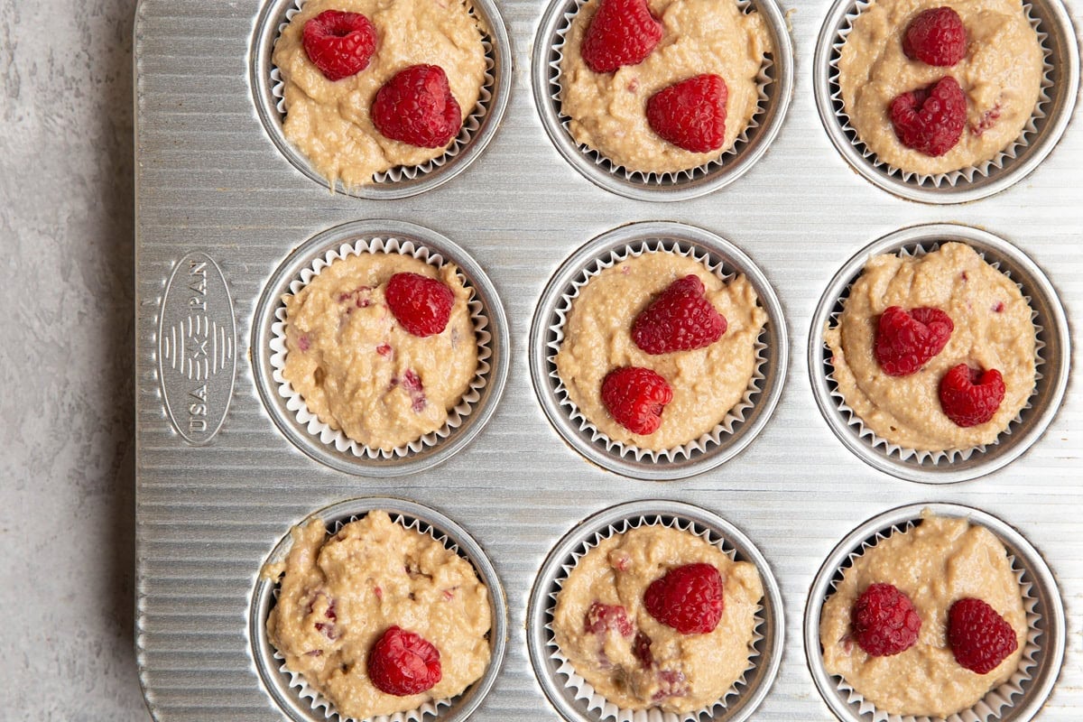 Muffin tray with raspberry muffin batter inside, ready to be baked.
