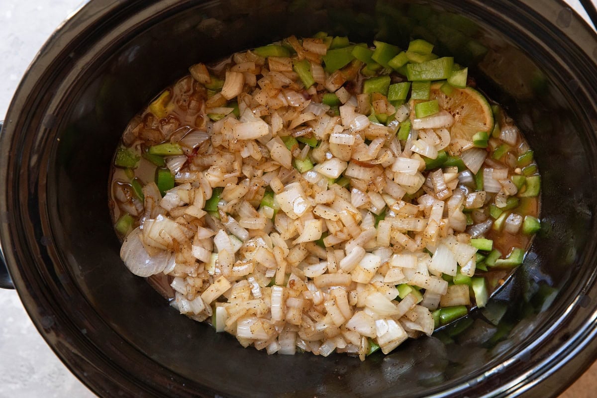 Crock pot full of liquid, seared chuck roast, sauteed onions, and bell peppers.