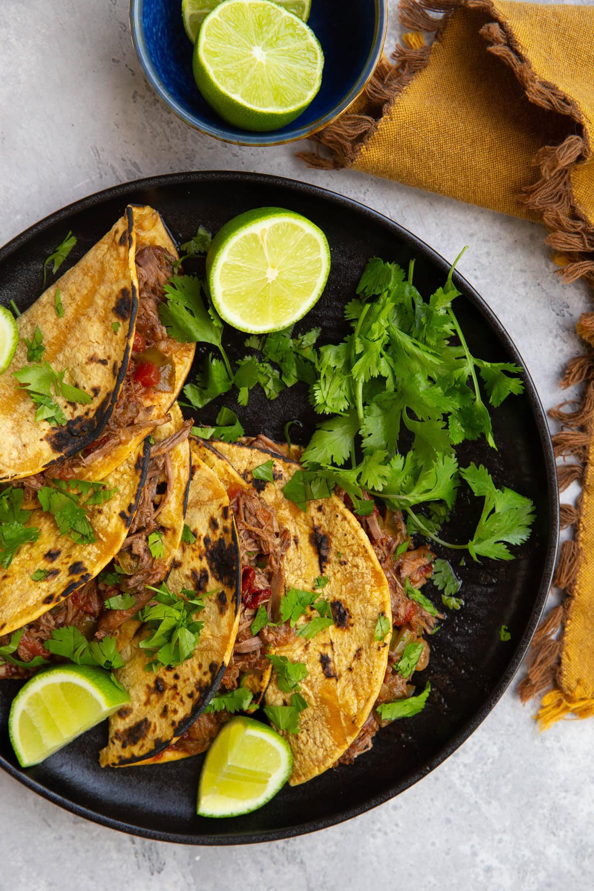 Black plate of four machaca tacos with toasted corn tortillas, fresh cilantro, and fresh limes.