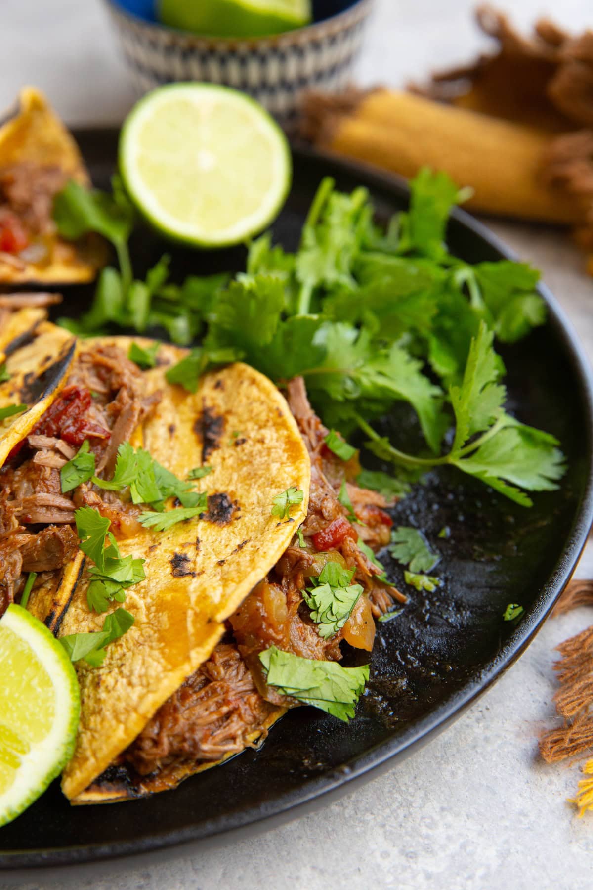 Beef machaca tacos on a black plate with fresh cilantro and limes, ready to serve.