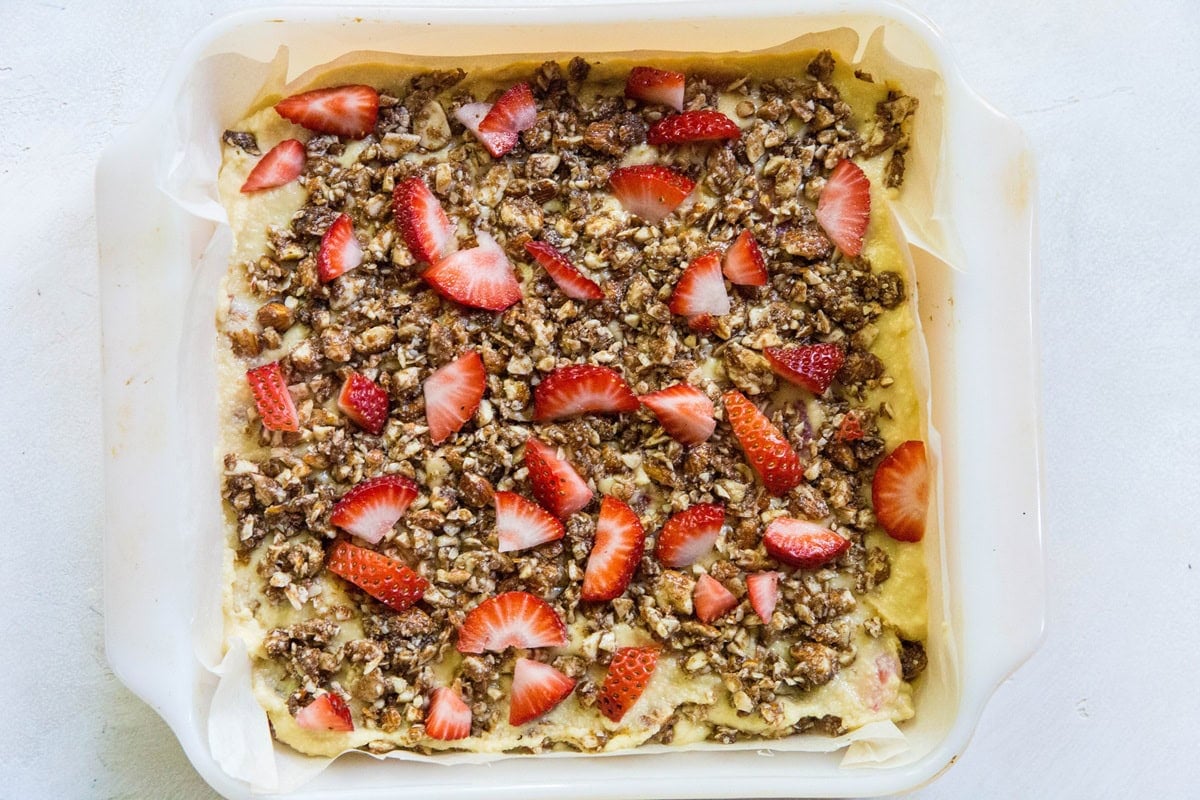 Cake pan with cake batter and streusel topping with chopped strawberries on top.
