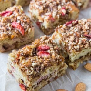 Strawberry crumb cake cut into slices on a cutting board with almonds to the side.