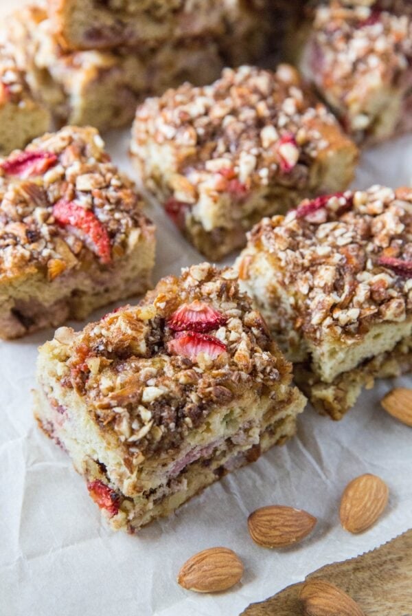 Strawberry crumb cake cut into slices on a cutting board with almonds to the side.