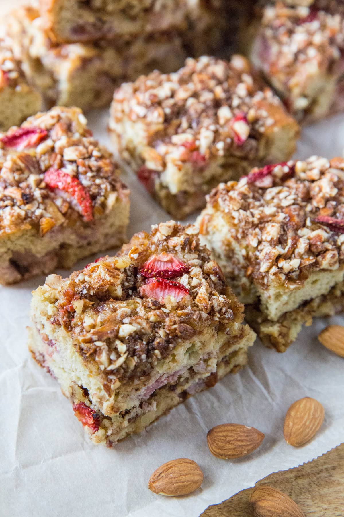 Strawberry crumb cake cut into slices on a cutting board with almonds to the side.