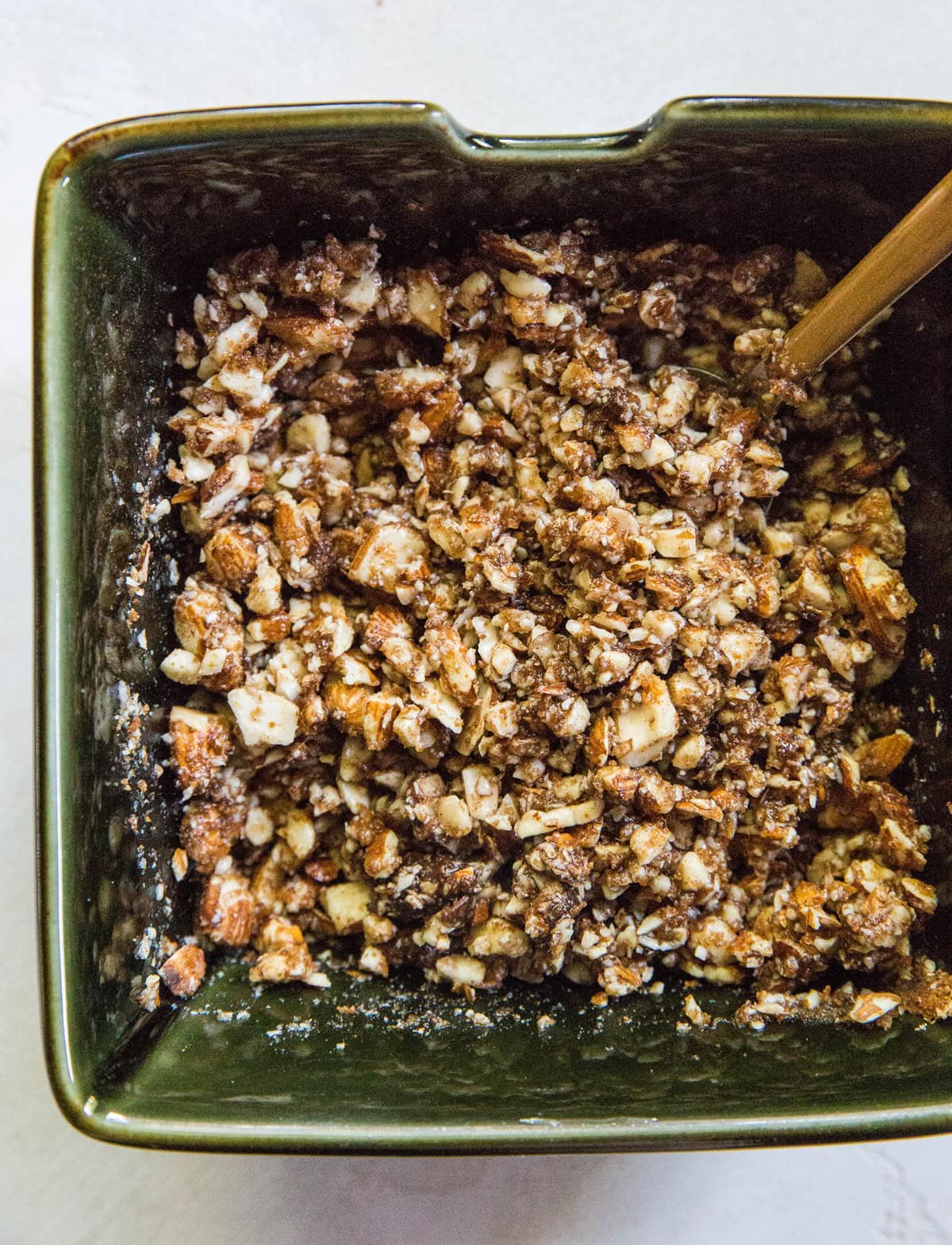 Almond topping in a green square bowl mixed up with a spoon.