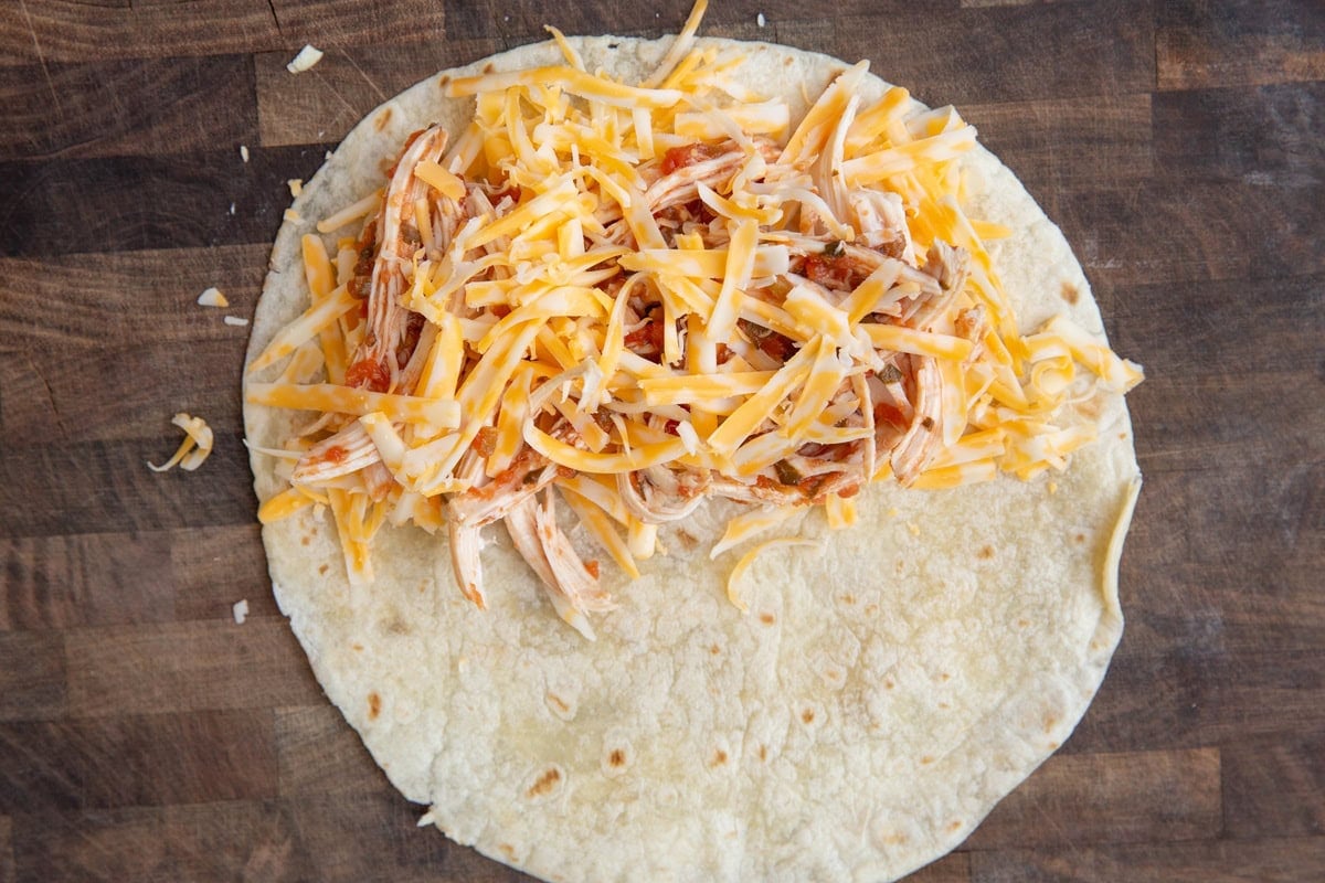 Tortilla with shredded cheese and shredded chicken over half of the tortilla.