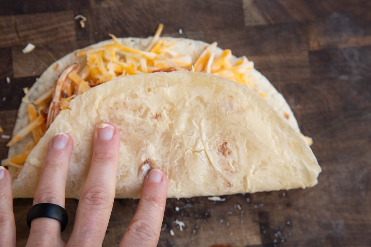 Hand folding tortilla over shredded cheese and chicken