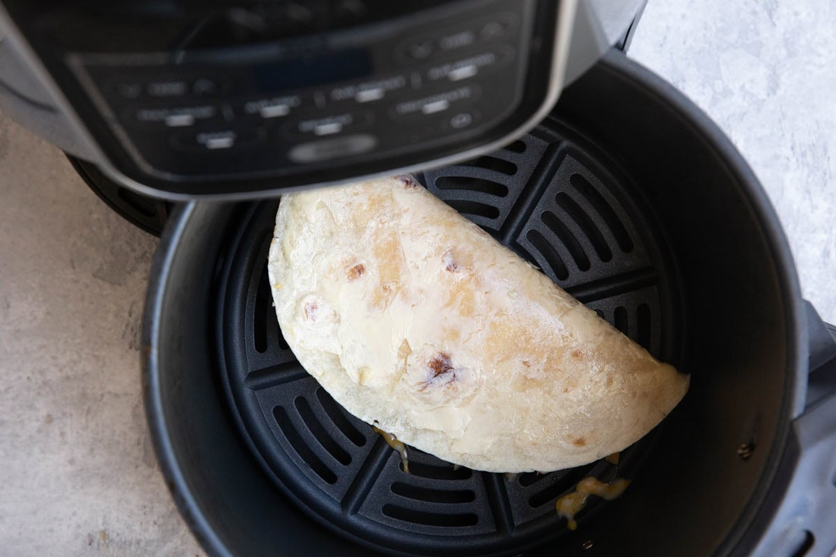 Air fryer with a half quesadilla inside with buttered tortilla on the outside.