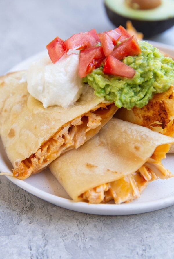 Three slices of chicken and cheese quesadilla with sour cream and guacamole on top.
