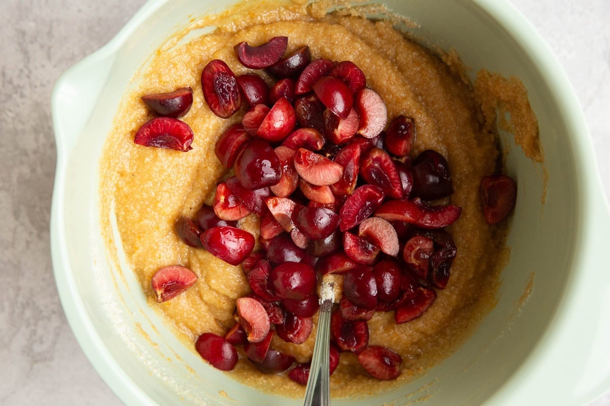 Mixing bowl full of cake batter with chopped cherries on top to be mixed in.